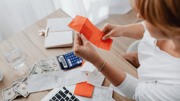 A person sitting at a desk reviewing receipts and organizing bills, with cash, a calculator, and a notebook nearby. This scene represents tracking expenses and financial planning to maintain a Realistic budget.