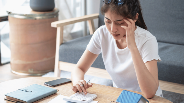 Young woman looking stressed while calculating finances, representing the challenges of Student Loan Repayment and budgeting.